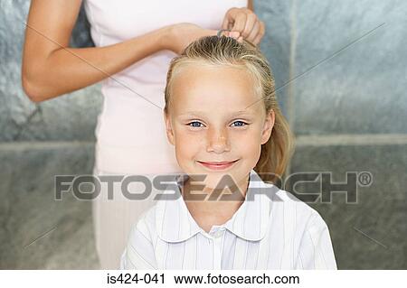 Stock Image - Mother tying her daughters hair back. Fotosearch