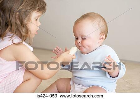 Sister feeding a baby a banana View Large Photo Image Stock Photo - Sister feeding a baby a banana. Fotosearch