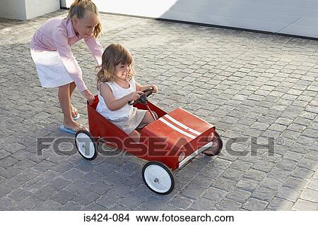 Sister pushing her younger sister in a toy car View Large Photo Image Picture - Sister pushing her younger sister in a toy car. Fotosearch