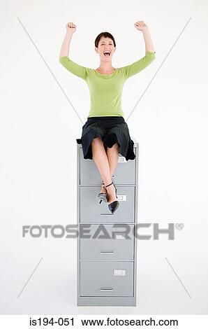 Stock Image - Woman sat on top of a filing cabinet. Fotosearch