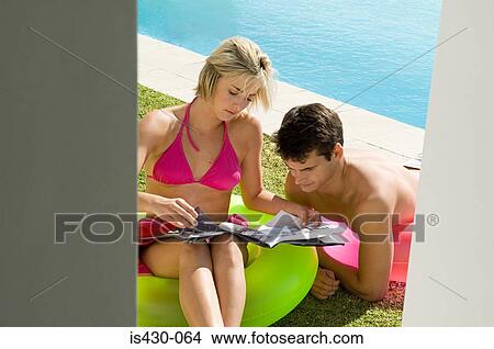 Couple reading a magazine by the pool View Large Photo Image Picture - Couple reading a magazine by the pool. Fotosearch