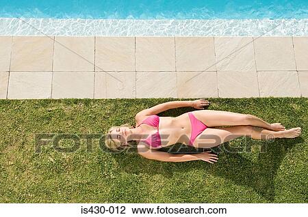 Stock Image - Woman sunbathing by pool. Fotosearch