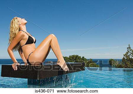 Stock Image - Woman sitting on platform in pool. Fotosearch
