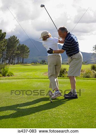 Stock Image - Man giving woman a golf lesson. Fotosearch