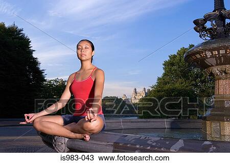 Stock Image - Woman meditating by fountain. Fotosearch