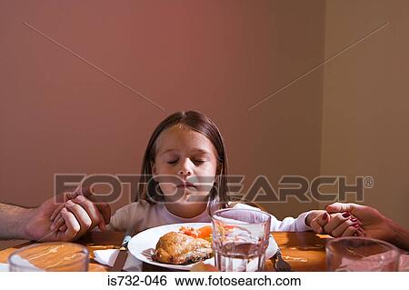 Stock Photograph - Family holding hands at dinner table. Fotosearch