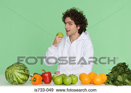 Stock Photo - Young man with fruit and vegetables on a table. Fotosearch