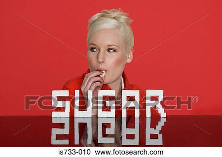 Stock Image - Young woman eating a sugar lump. Fotosearch