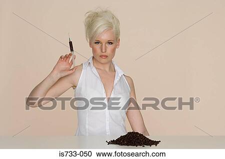 Stock Image - Young woman holding a syringe filled with coffee. Fotosearch