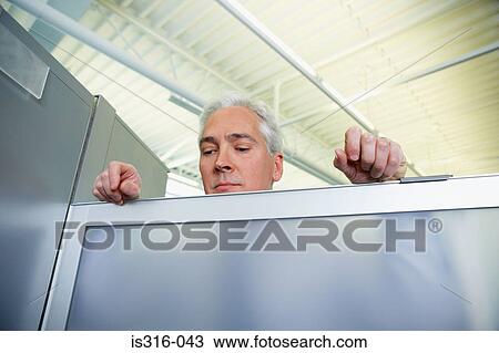 Stock Image - Man peering over a glass partition. Fotosearch