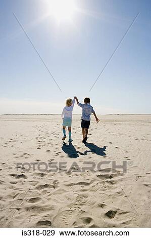 Stock Photo - Boy and girl walking on beach holding hands. Fotosearch