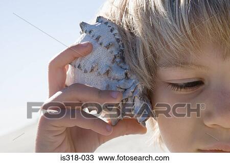 Stock Image - Boy holding shell to ear. Fotosearch
