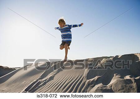 Stock Image - Boy jumping on sand dune. Fotosearch