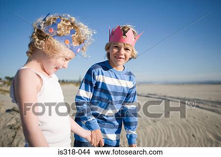 Picture - Brother and sister wearing paper crowns holding hands. Fotosearch