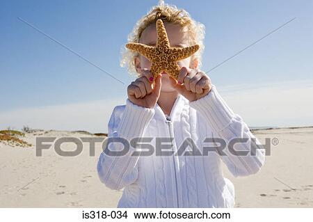 Girl holding starfish in front of face View Large Photo Image Picture - Girl holding starfish in front of face. Fotosearch