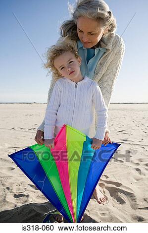 Stock Image - Grandmother and granddaughter playing with kite on beach. Fotosearch