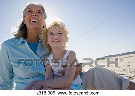 Stock Photograph - Grandmother and granddaughter sitting on beach. Fotosearch