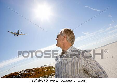 Stock Photography - Senior man on beach looking at plane. Fotosearch