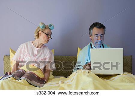 Picture - Couple in bed with laptop and magazine. Fotosearch