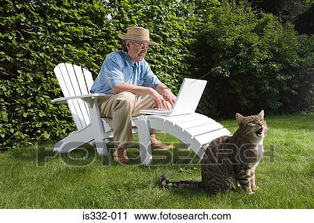 Stock Image - Man in garden with laptop and cat. Fotosearch