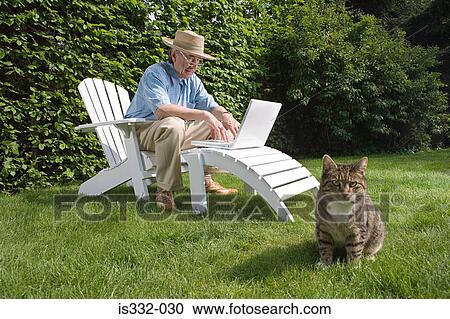 Stock Image - Man in garden with laptop and cat. Fotosearch