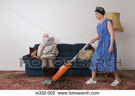 Man reading newspaper as woman vacuums View Large Photo Image Stock Image - Man reading newspaper as woman vacuums. Fotosearch