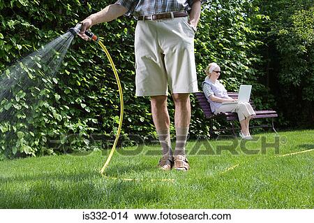 Picture - Man watering lawn and woman using laptop. Fotosearch