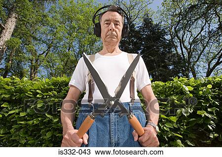 Stock Image - Man wearing headphones and holding gardening shears. Fotosearch