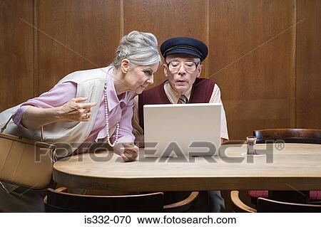 Stock Image - Senior couple in public house with laptop. Fotosearch