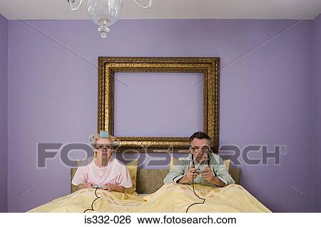 Stock Photograph - Senior couple playing video game in bed. Fotosearch