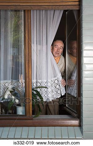 Stock Photo - Senior peering around net curtain. Fotosearch
