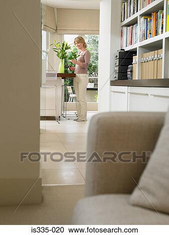 Stock Image - Woman arranging flowers in kitchen. Fotosearch