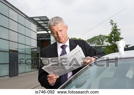 Stock Image - Businessman reading newspaper by car. Fotosearch