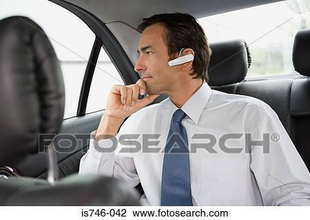 Stock Image - Businessman with bluetooth headset sitting in car. Fotosearch