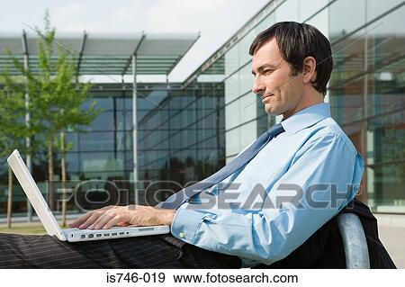 Stock Photo - Businessman with laptop on office courtyard. Fotosearch