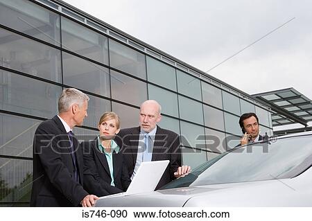 Stock Image - Businesspeople looking at laptop on automobile boot. Fotosearch