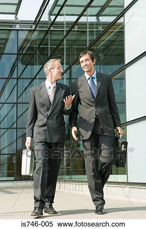 Stock Photography - Two businessman walking alongside office building. Fotosearch
