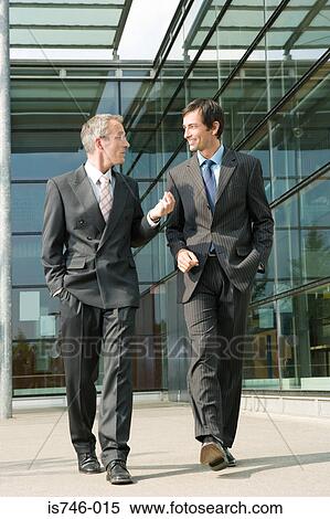 Two businessmen walking along office building View Large Photo Image Stock Photography - Two businessmen walking along office building. Fotosearch
