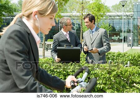Stock Photograph - Woman on bike, two businessmen on background. Fotosearch