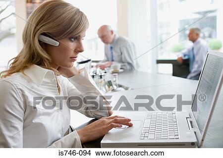 Picture - Woman wearing headset using laptop at bar counter. Fotosearch