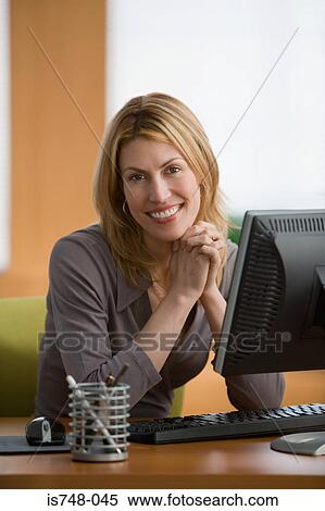 Stock Photography - Young woman sitting at desk. Fotosearch