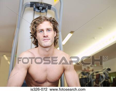 Stock Image - Man sitting at exercising equipment . Fotosearch