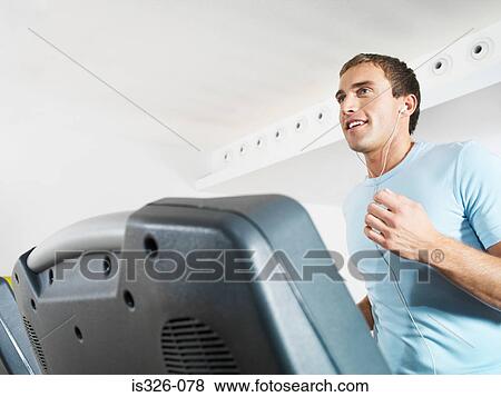 Man wearing earphones on treadmill in health club View Large Photo Image Stock Photo - Man wearing earphones on treadmill in health club . Fotosearch