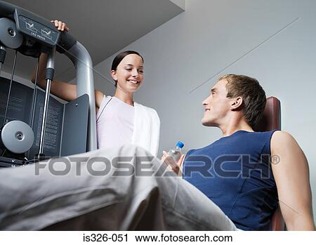 Stock Image - Man weight training woman assisting . Fotosearch