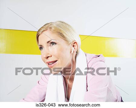 Stock Image - Woman with earphones on exercise bike in health club. Fotosearch