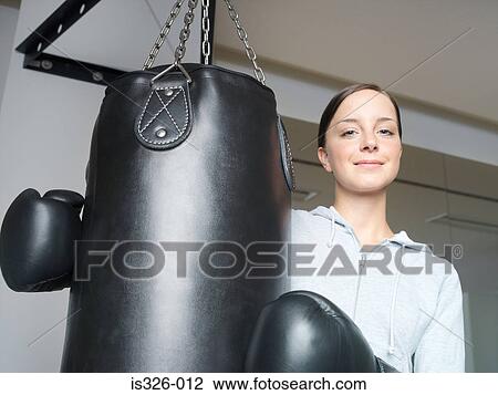 Stock Image - Young female boxer with gloves at punch bag . Fotosearch