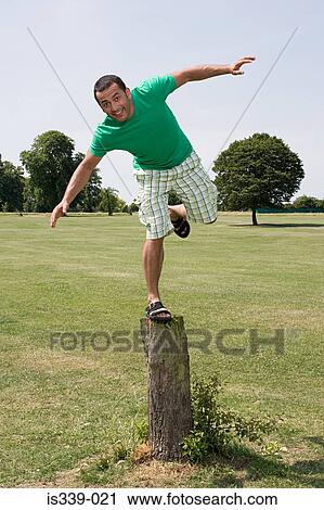 Stock Image - Man balancing on tree stump. Fotosearch
