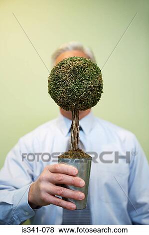 Stock Photo - Man holding bonsai tree in front of his face. Fotosearch