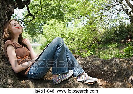Girl sitting on a tree trunk View Large Photo Image Stock Photograph - Girl sitting on a tree trunk. Fotosearch