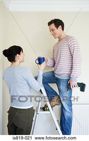 Stock Image - Woman handing coffee to husband on stepladder. Fotosearch